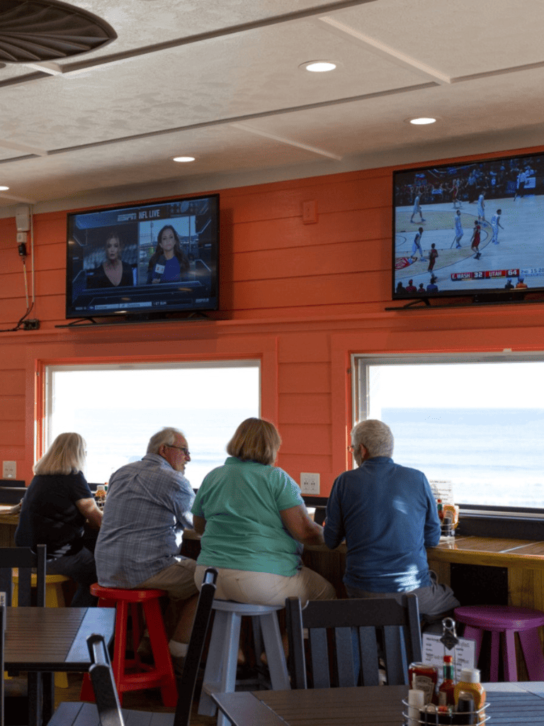 Watching sports on multiple TVs at a lively bar, enjoying drinks and snacks with friends, vibrant atmosphere for sports fans.