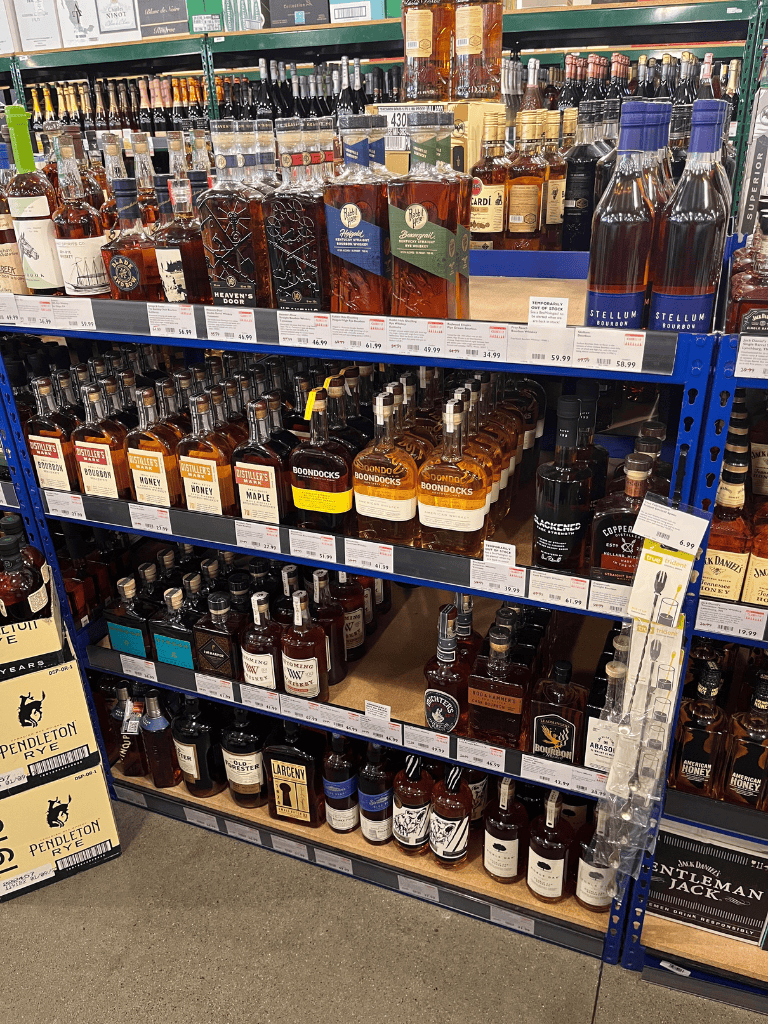 Aisle of whiskey bottles on retail store shelves for sale.