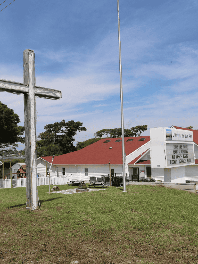 Colorful church with cross and sign at seaside, offering weekly service and spiritual guidance.