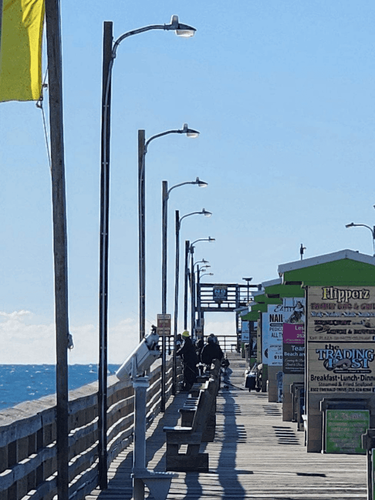 Brightly lit seaside pier with street lamps, seating, and shops along the oceanfront, perfect for strolling and enjoying the view.