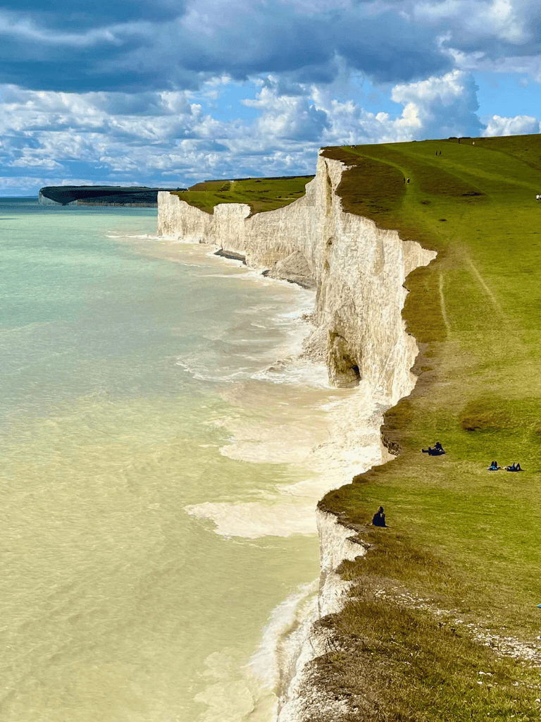 Stunning white chalk cliffs along the coast with lush green grass and people relaxing on the edge.
