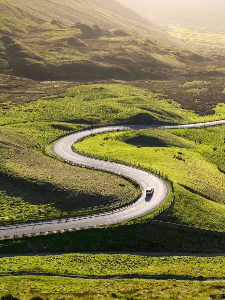 Winding mountain road through lush green hills in scenic countryside.