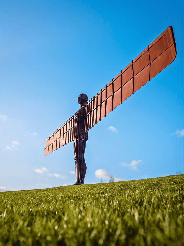 Windmill sculpture against a blue sky surrounded by lush green grass, symbolizing innovation and eco-friendly energy solutions.