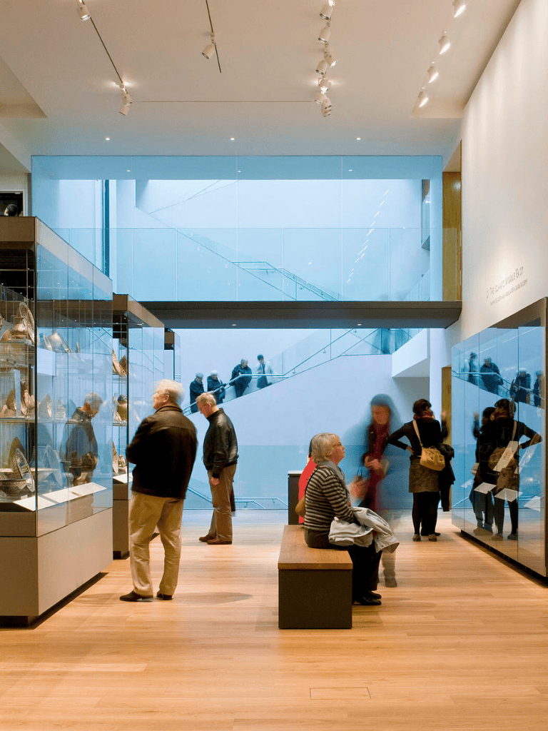 Bright modern museum interior with visitors exploring art and artifacts, sleek glass display cases, and a spacious, light-filled environment.