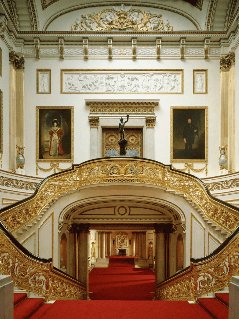 Opulent palace staircase with intricate gold railing and classical portraits, grand architecture, and ornate decor.