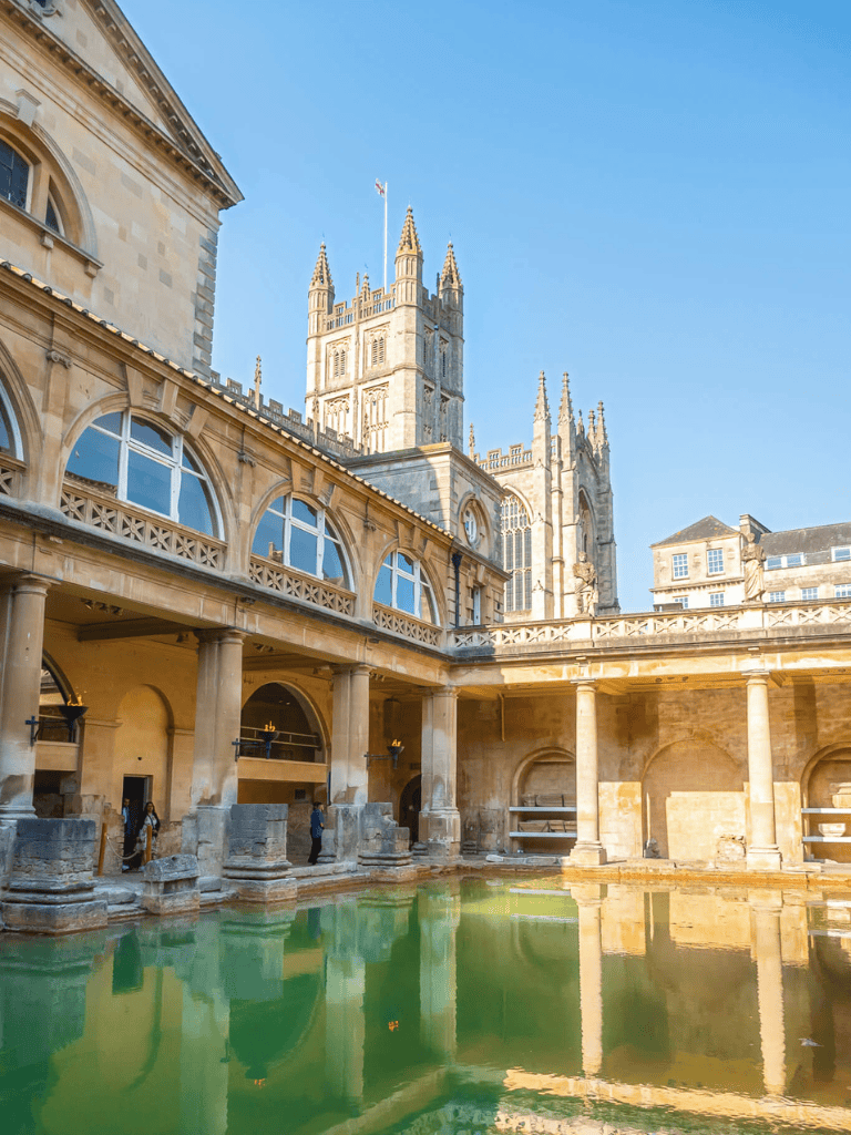 Ancient Bathhouse with historic architecture, water pool, and Gothic cathedral in the background.