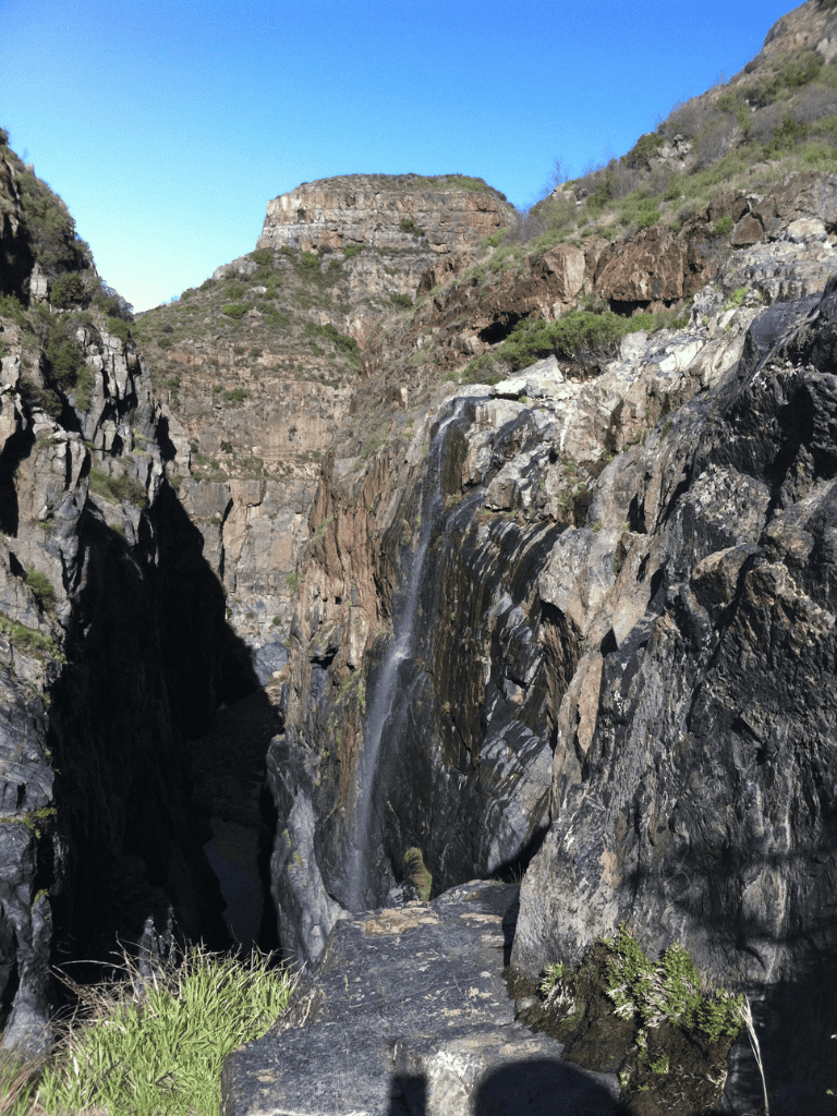 Waterfall cascading down rocky canyon at QuestForDirections outdoor trail.