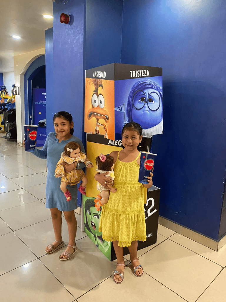 Smiling girls holding Coca-Cola drinks at an emotional movie-themed display.