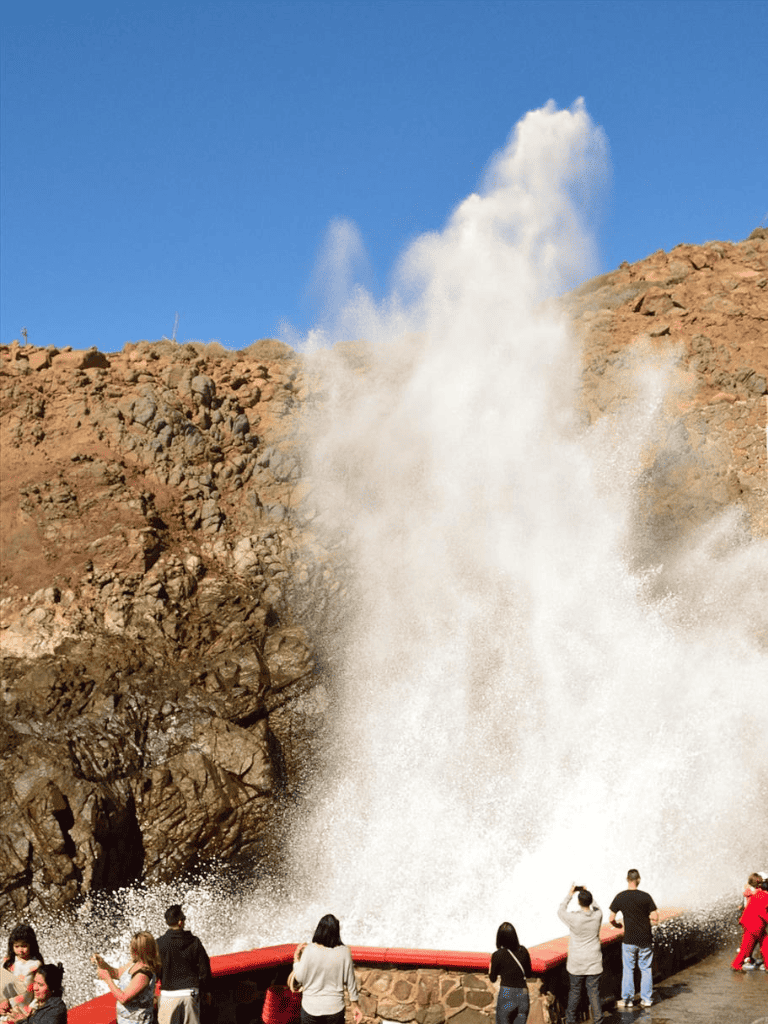 Massive geyser eruption at geothermal park, tourists watch water and steam blast into the sky.