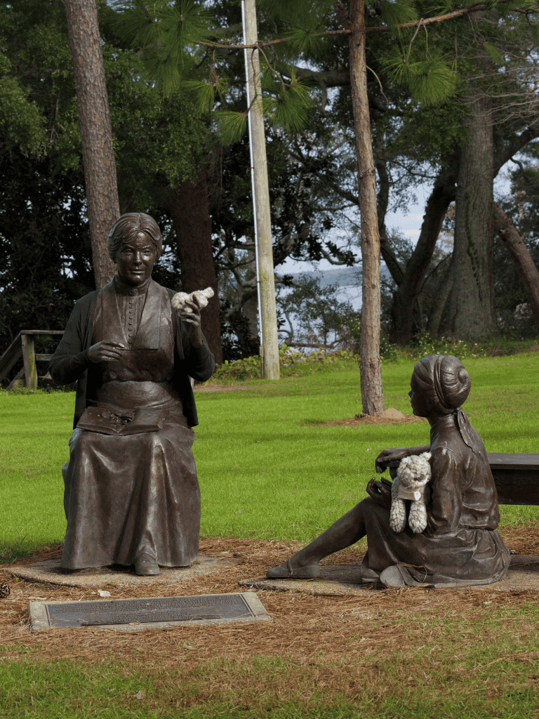 Old-fashioned woman and girl bronze statues at QuestForDirections park, representing historical community scenes.