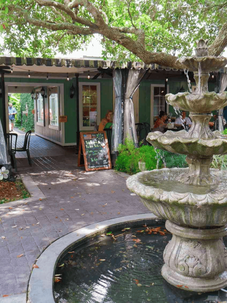 Charming outdoor cafe with water fountain and lush greenery, perfect for relaxing dining experience.