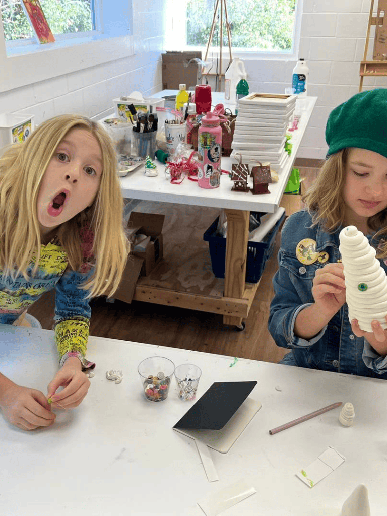 Colorful craft supplies on table, children creating holiday decorations in classroom.