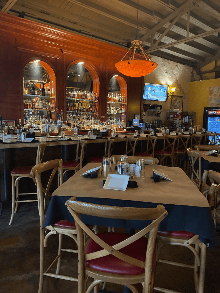 Elegant bar and dining area with a well-stocked liquor shelf, cozy lighting, and inviting table settings for a memorable night out.