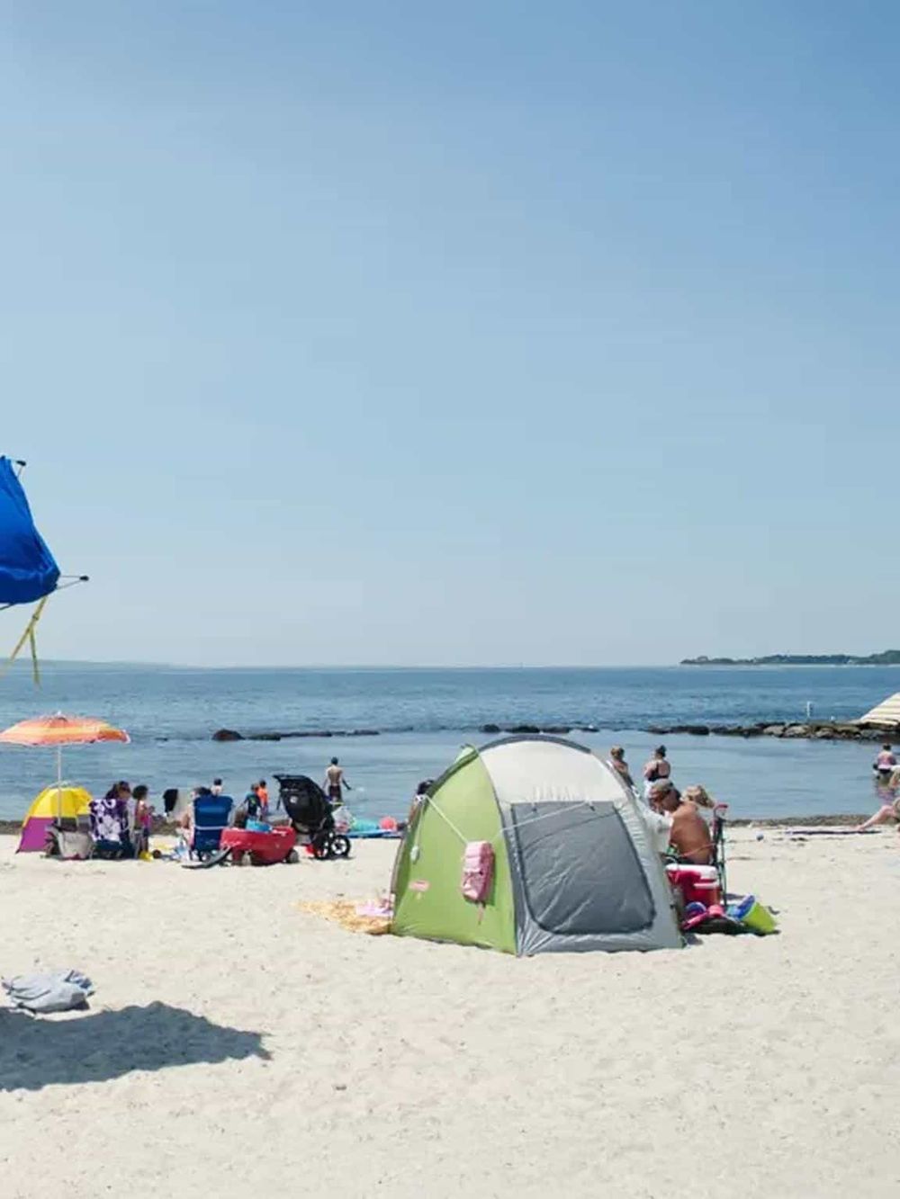Sunny beach scene with people, umbrellas, and a tent by the ocean, perfect for travel and vacation SEO.
