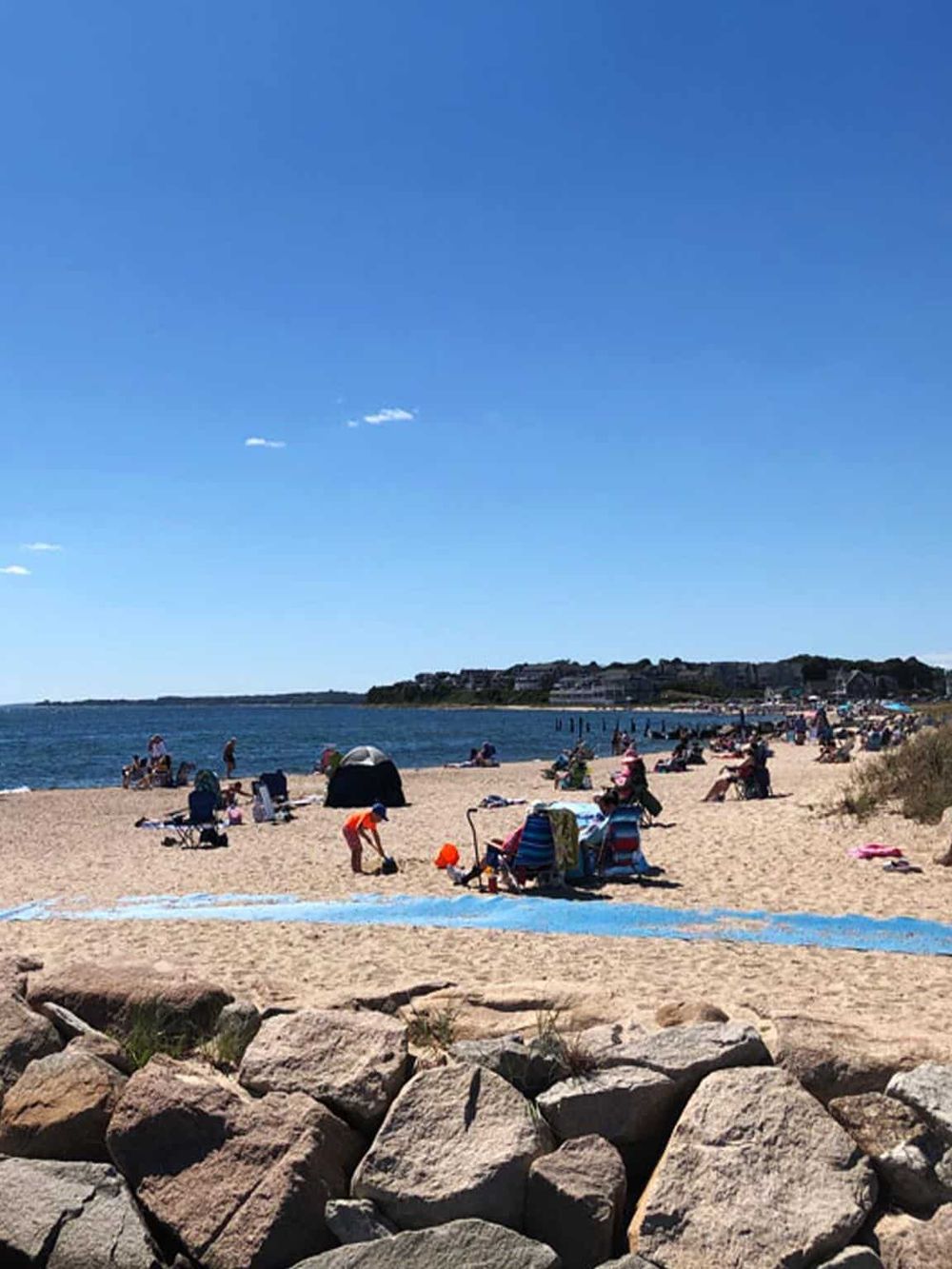 Bright sunny day at the beach with families and groups enjoying the sand and ocean view, perfect for relaxation and summer fun.
