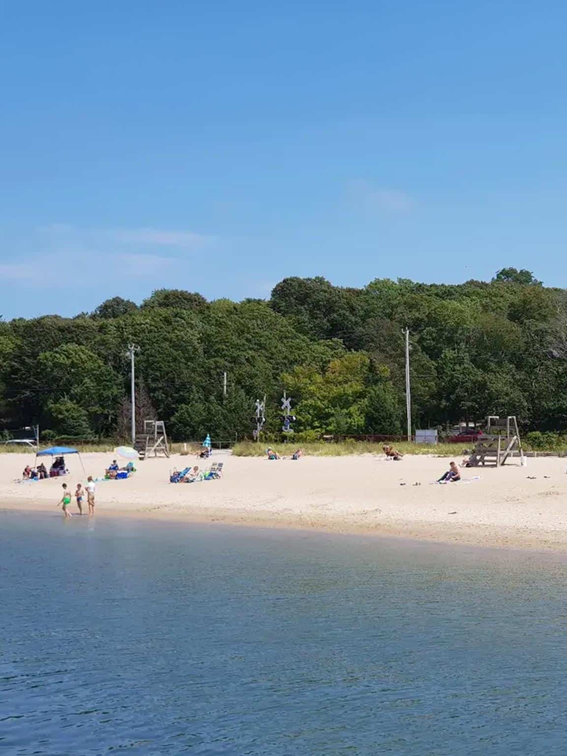 Scenic beach with white sand, clear water, and lush green trees in the background, perfect for relaxation and outdoor activities.