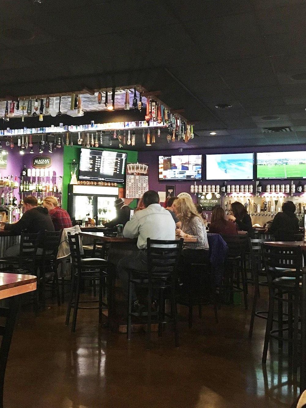 Cozy bar interior with multiple televisions, patrons enjoying drinks, and colorful decor, ideal for sports viewing and socializing.