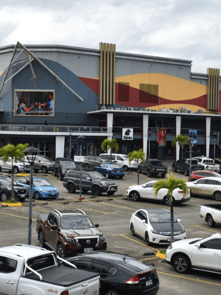 Bright shopping mall parking lot with numerous vehicles and colorful exterior design.