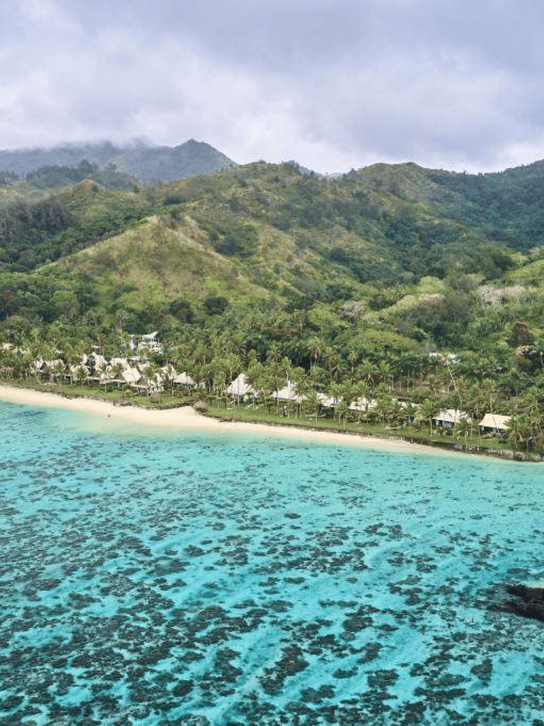 Stunning tropical beach with overwater bungalows and lush green mountains in the background.