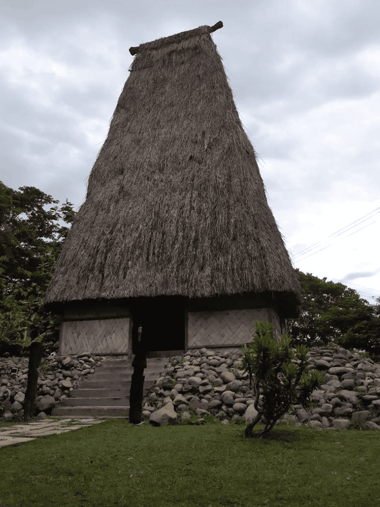 Traditional thatched hut on a grassy landscape with cloudy sky in the background.