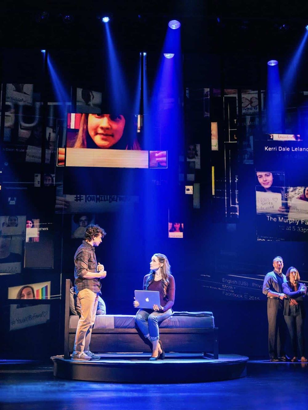 Interactive theater performance with actors on stage and digital screens in the background.