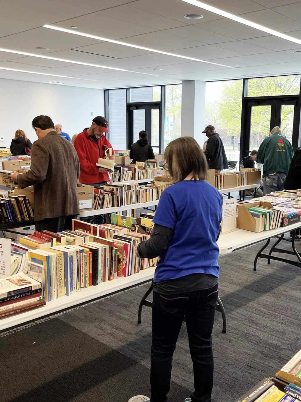 Wide indoor bookstore with customers browsing books, bright natural light, modern design, and diverse selection of genres.|Bookshelves filled with diverse books in a bright, modern bookstore attracting readers.