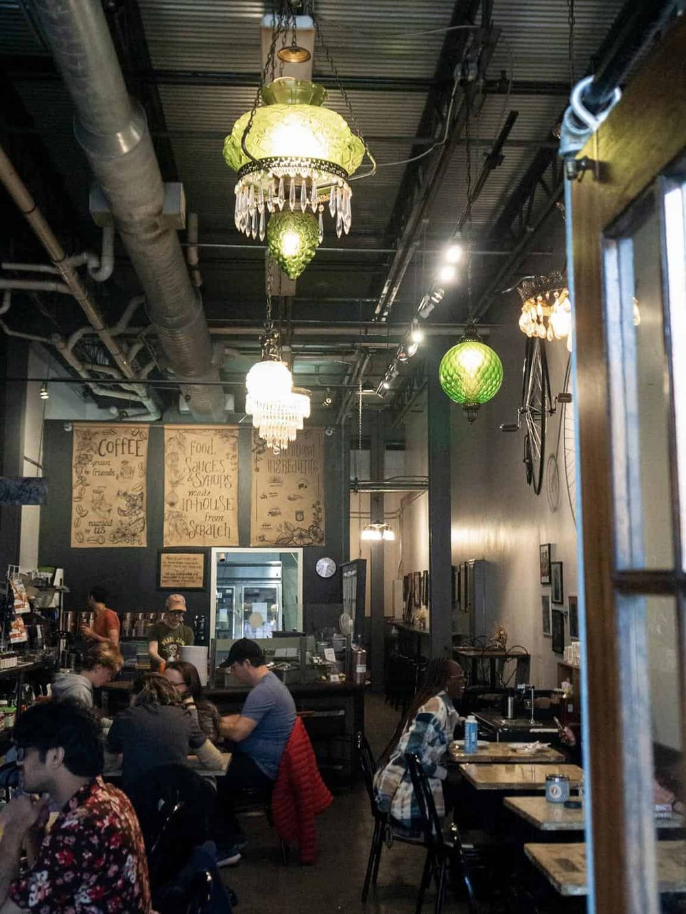 Colorful boho-style pendant lights in a cozy coffee shop interior filled with customers.