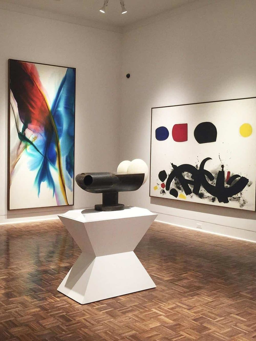Colorful abstract artwork at modern art gallery with sculpture on white pedestal.