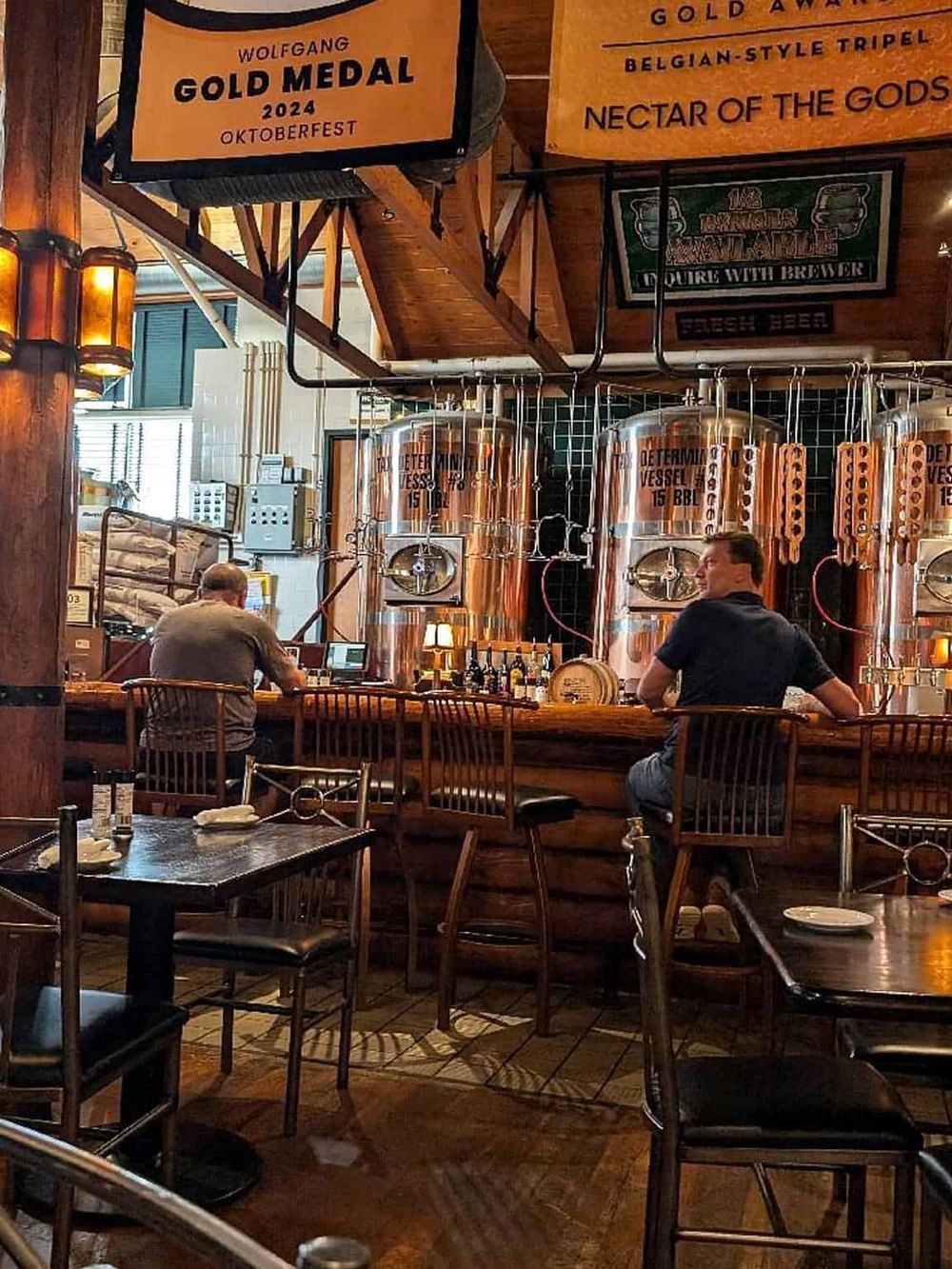 Copper brewing tanks at a brewery with patrons sitting at the bar, showcasing craft beer and brewery tour experiences.