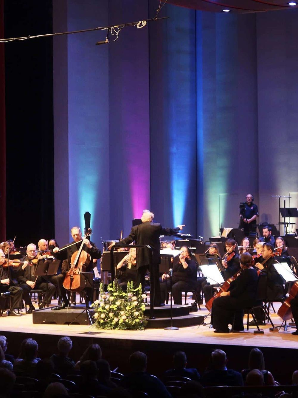 Orchestra performing live on stage at QuestForDirections event, vibrant colorful lighting, conductor directing musicians.