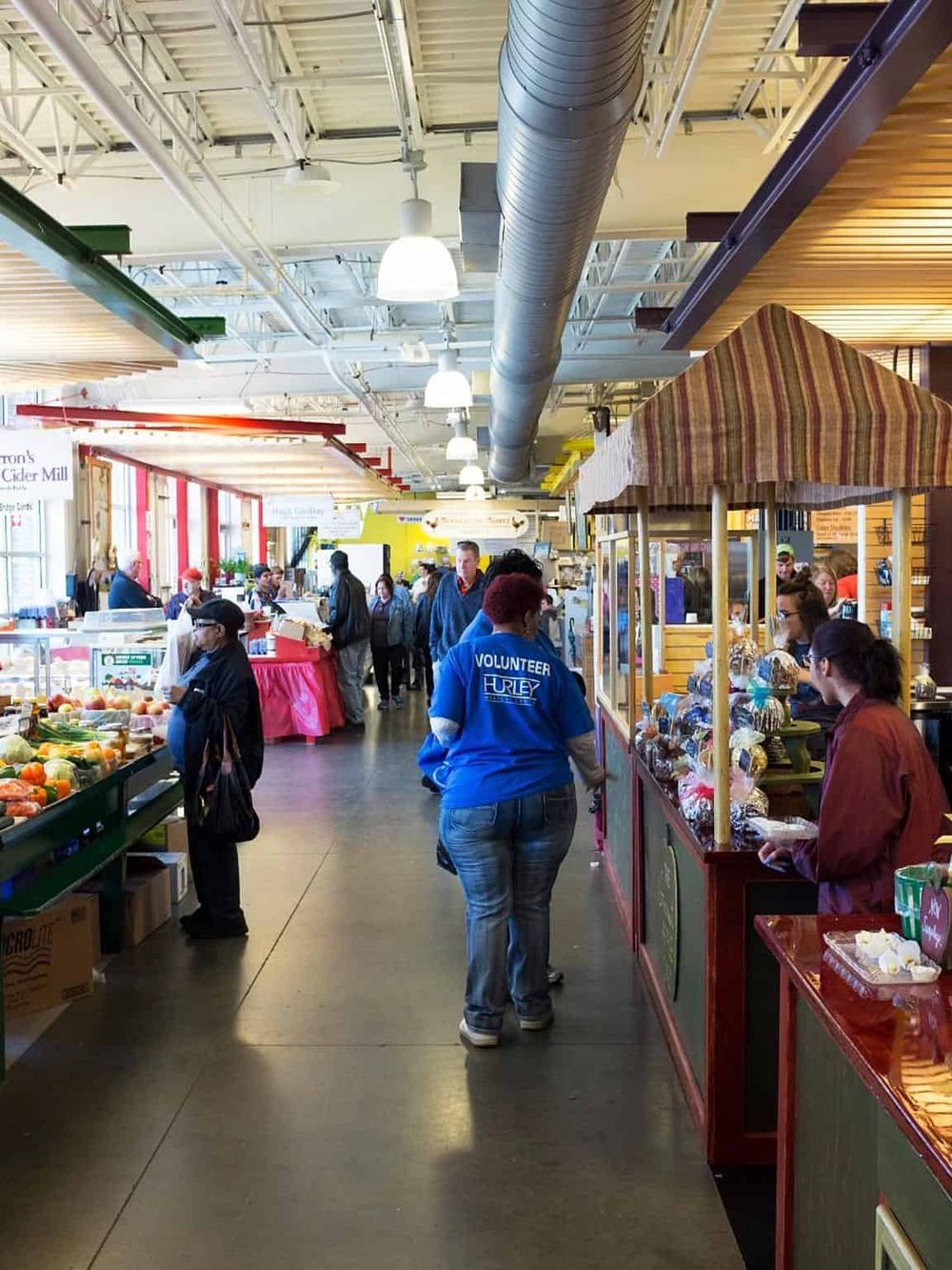 Vibrant farmers market indoor scene with vendors, shoppers, fresh produce, and handcrafted goods.