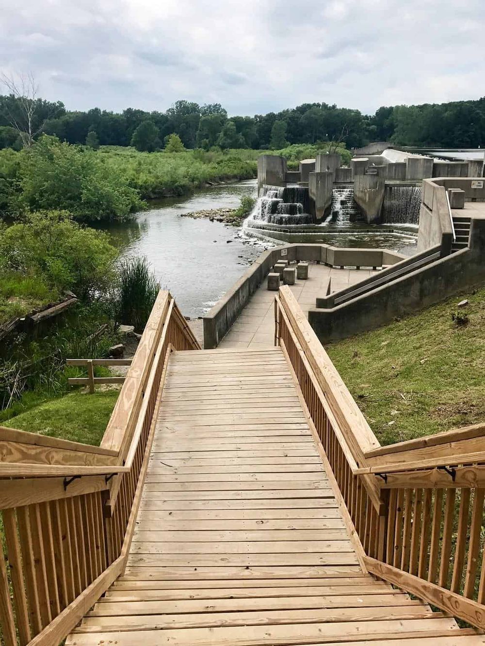 River dam and walkway at QuestForDirections outdoor park spot with lush greenery, ideal for nature navigation.