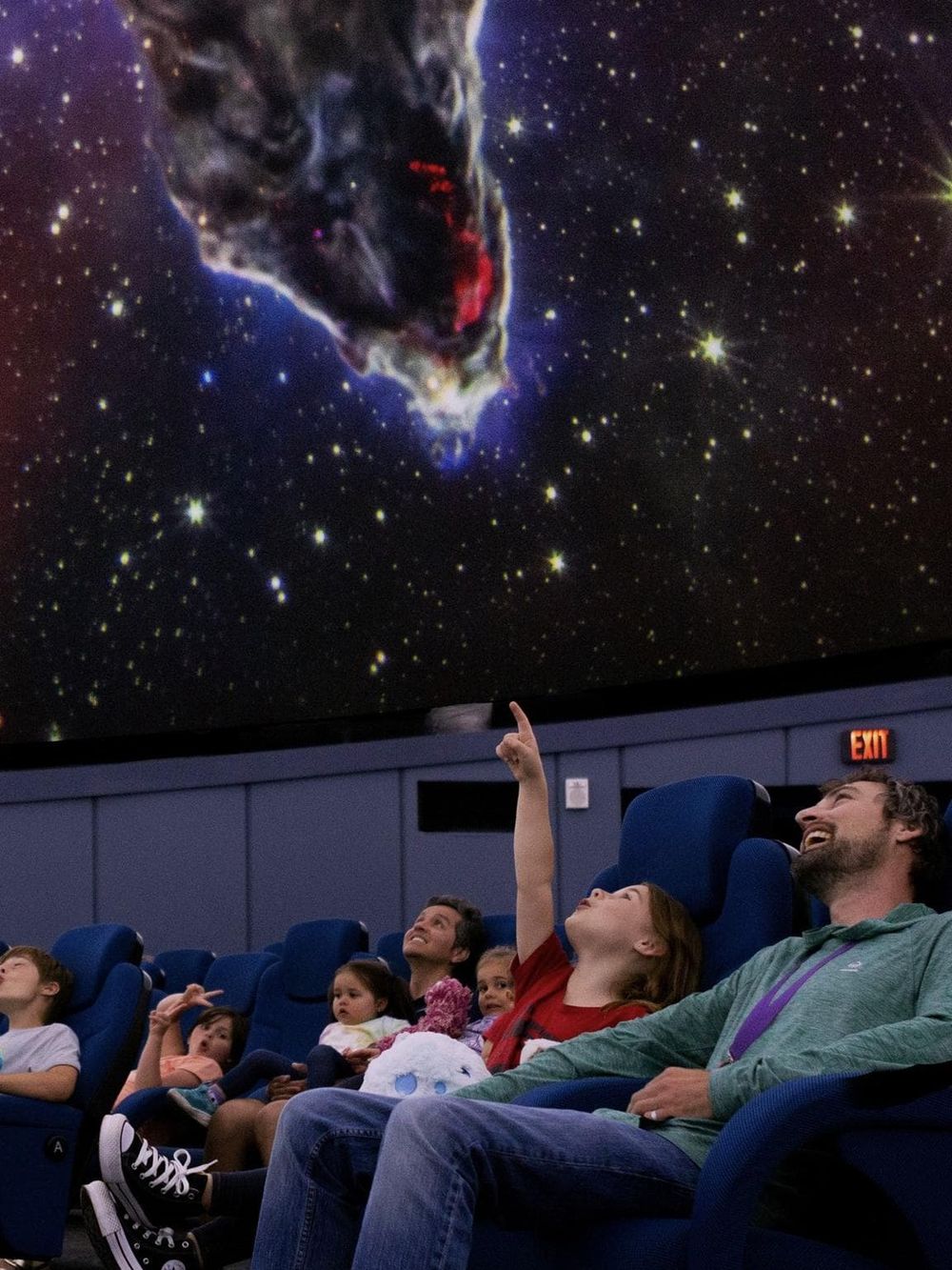 Vast starry sky at an observatory with a family watching an astronomy presentation on a large screen.