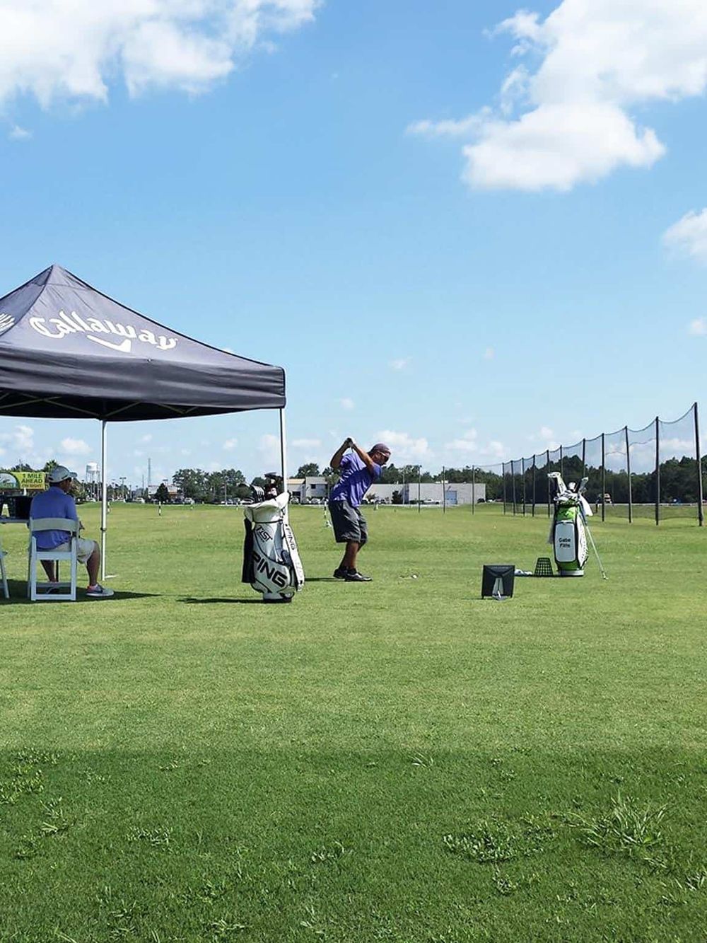 1. Golf practice area with golfers, tents, and caddies on a sunny day.