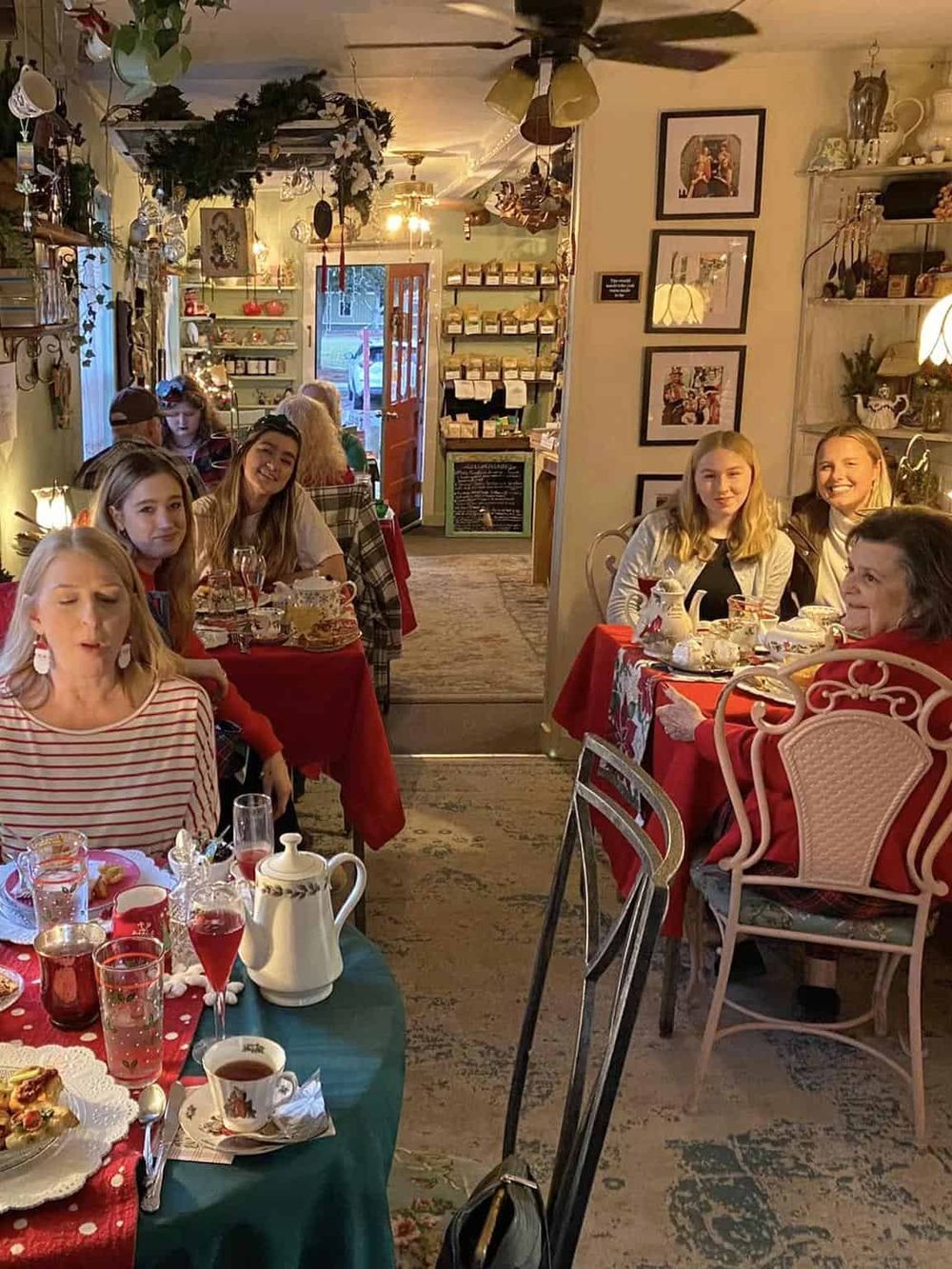 Warm cozy cafe interior with holiday decorations, group enjoying tea, desserts, and festive ambiance.