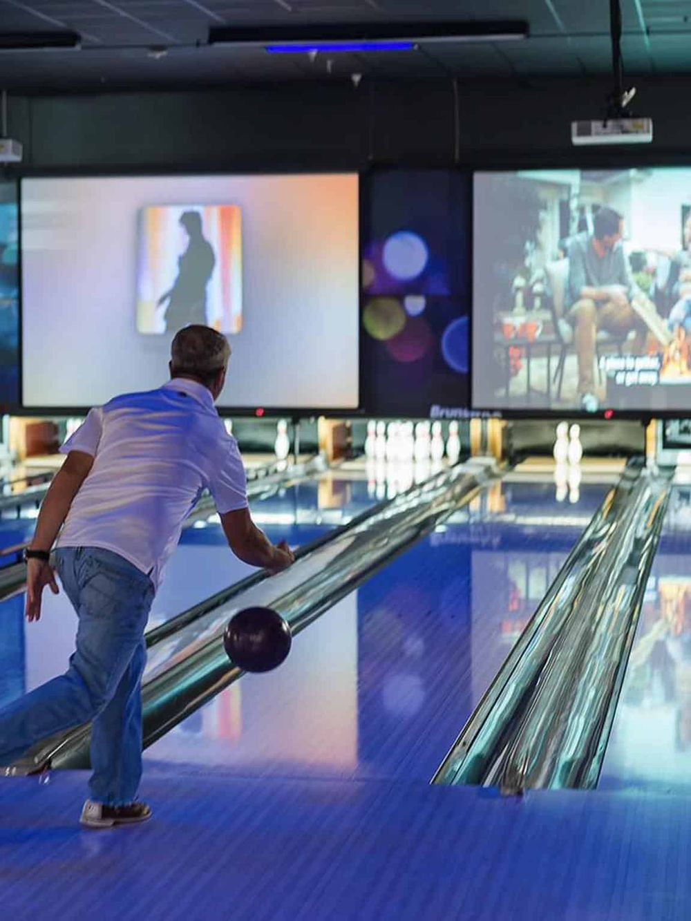1. Person bowling in a modern indoor bowling alley with large screens displaying art and images.