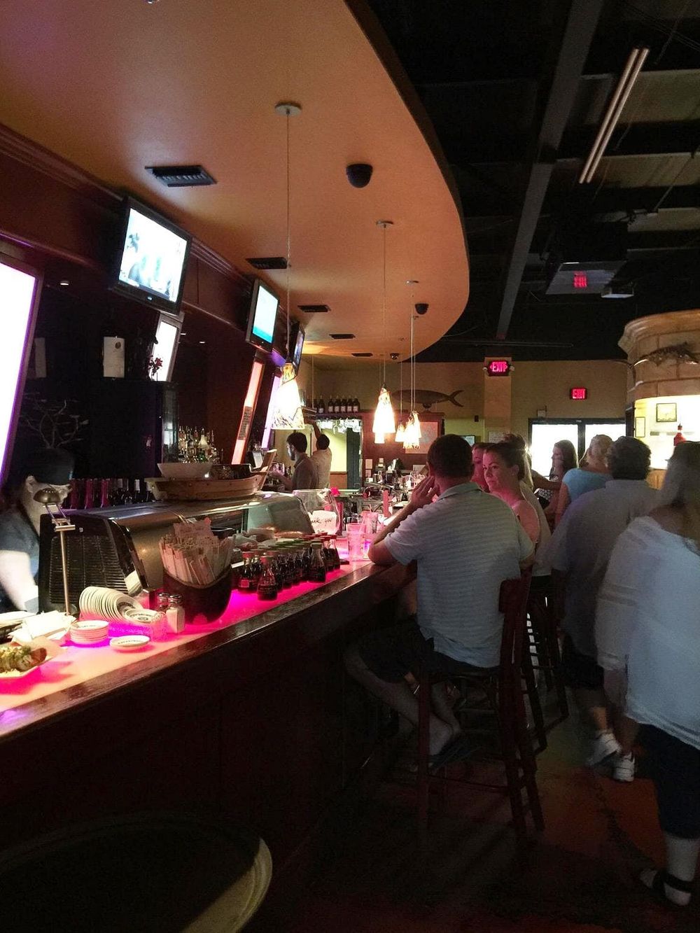 People at a bar with multiple TVs, dim lighting, and a lively social ambiance, perfect for dinner or drinks.