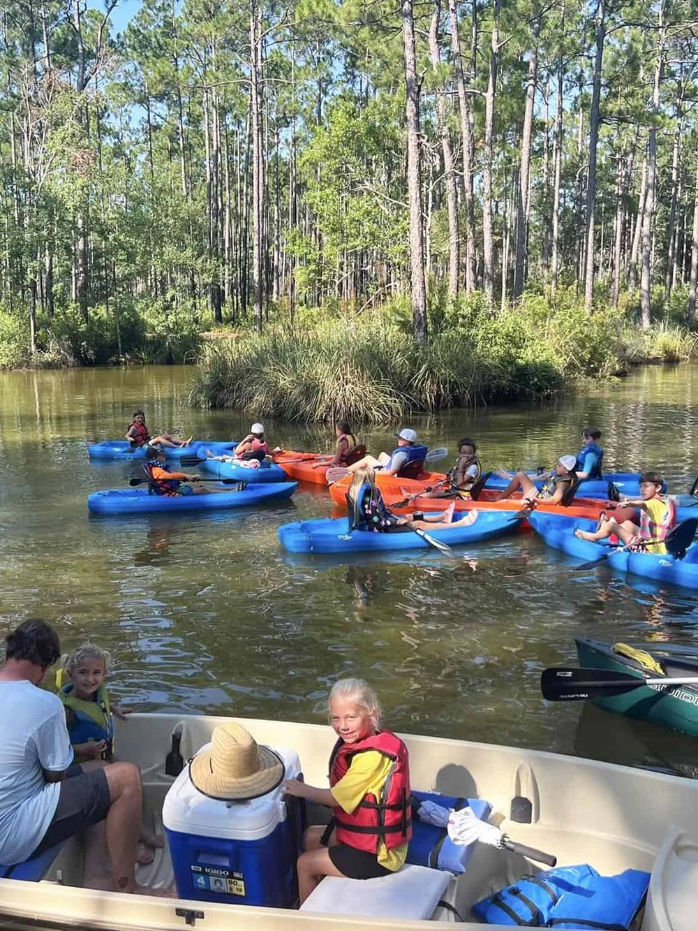 Kayaking on a calm river with a group of children and adults surrounded by lush green trees.