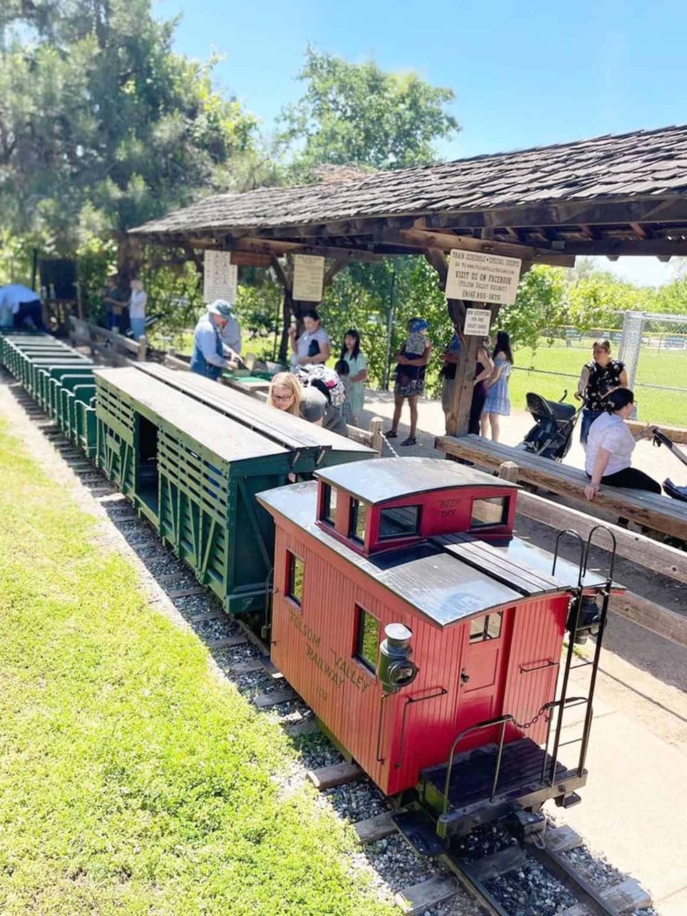 Colorful miniature train at a park with people waiting to ride, emphasizing family-friendly attractions and outdoor adventures.