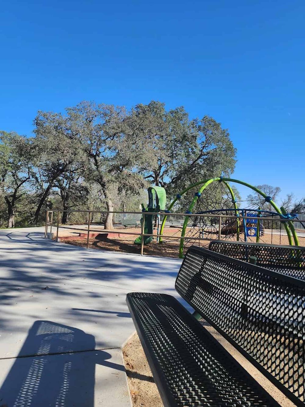 Bright sunny park with playground, benches, large trees, and clear blue sky, perfect for outdoor recreation.