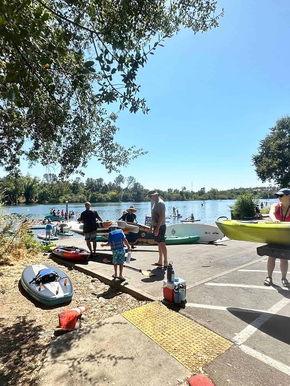 A vibrant lakeside scene featuring people preparing paddleboards and kayaks for a fun day on the water. Perfect for outdoor adventure and water sports enthusiasts.