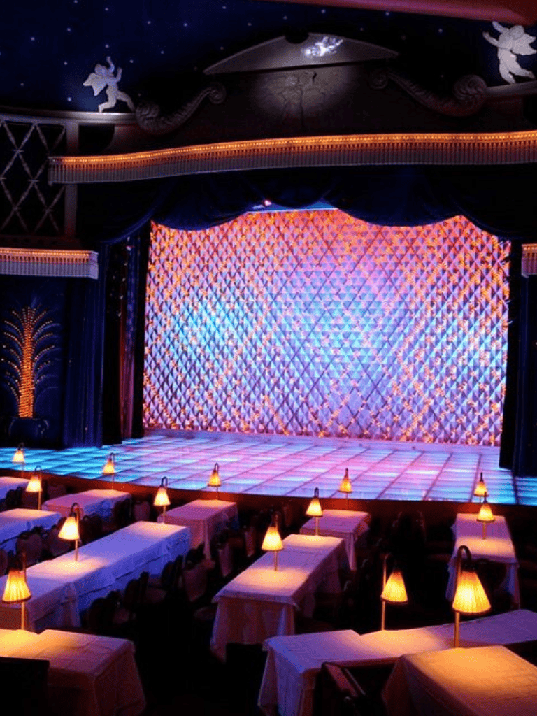 Bright theater stage with colorful lighting and elegant dining tables with small lamps.