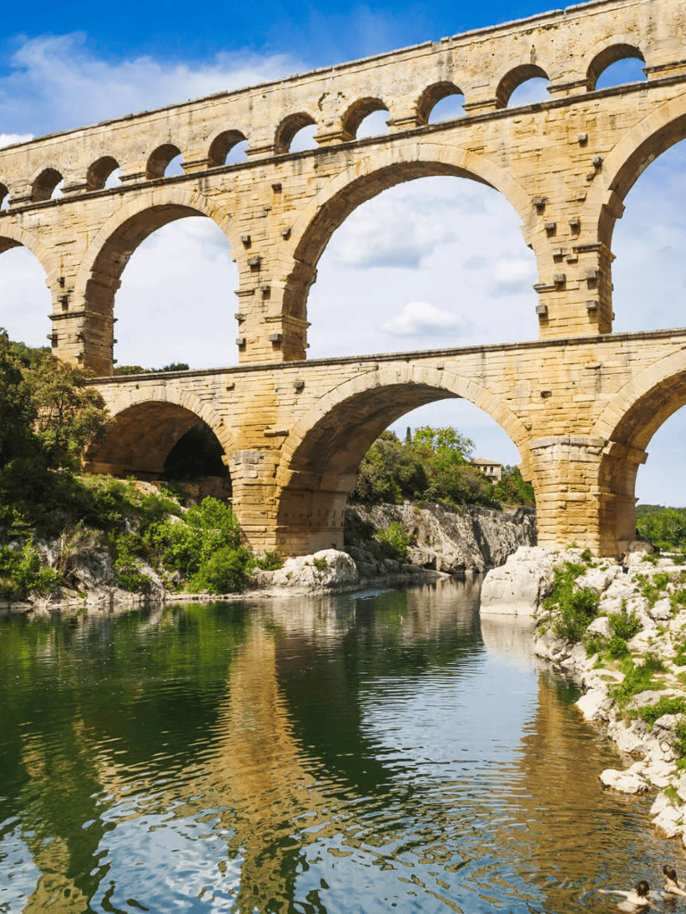 Ancient Roman aqueduct over a river with lush greenery, symbolizing historical engineering and scenic beauty.