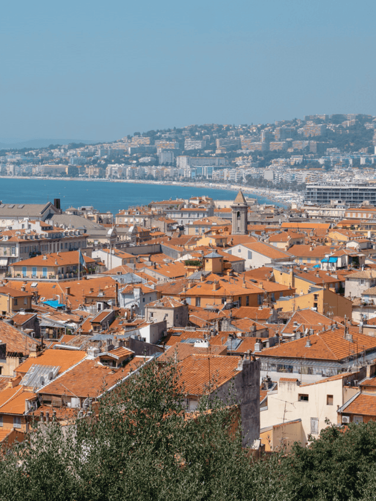 Panoramic view of coastal Mediterranean city with orange-tiled rooftops and sea in the background.