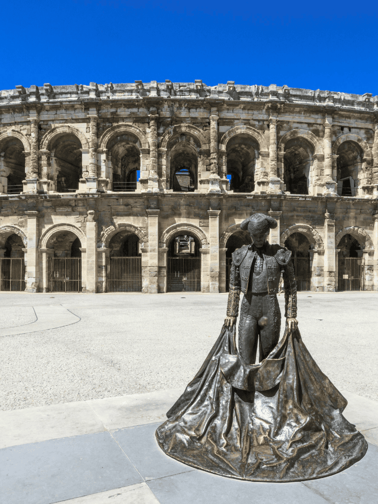 Bronze bullfighter statue outside ancient Roman amphitheater, historic cultural landmark and tourist attraction.