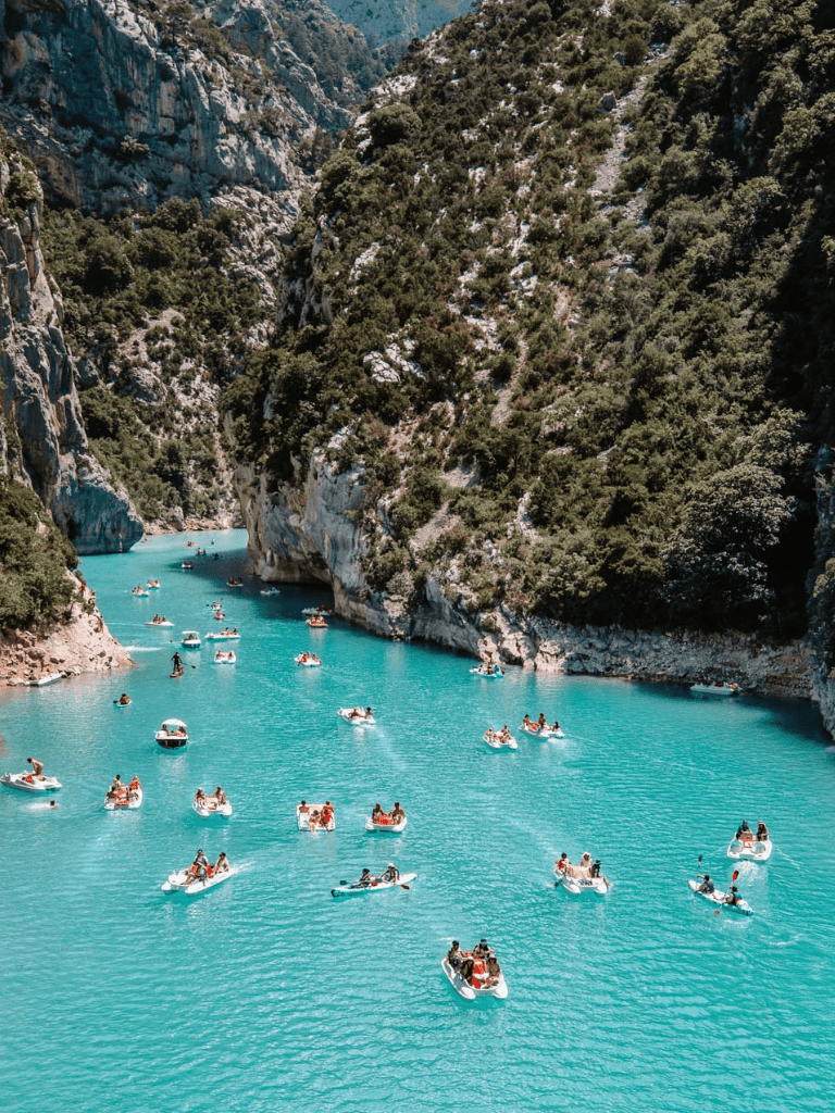 Colorful boats on turquoise river surrounded by cliffs and lush greenery, scenic outdoor adventure in nature.