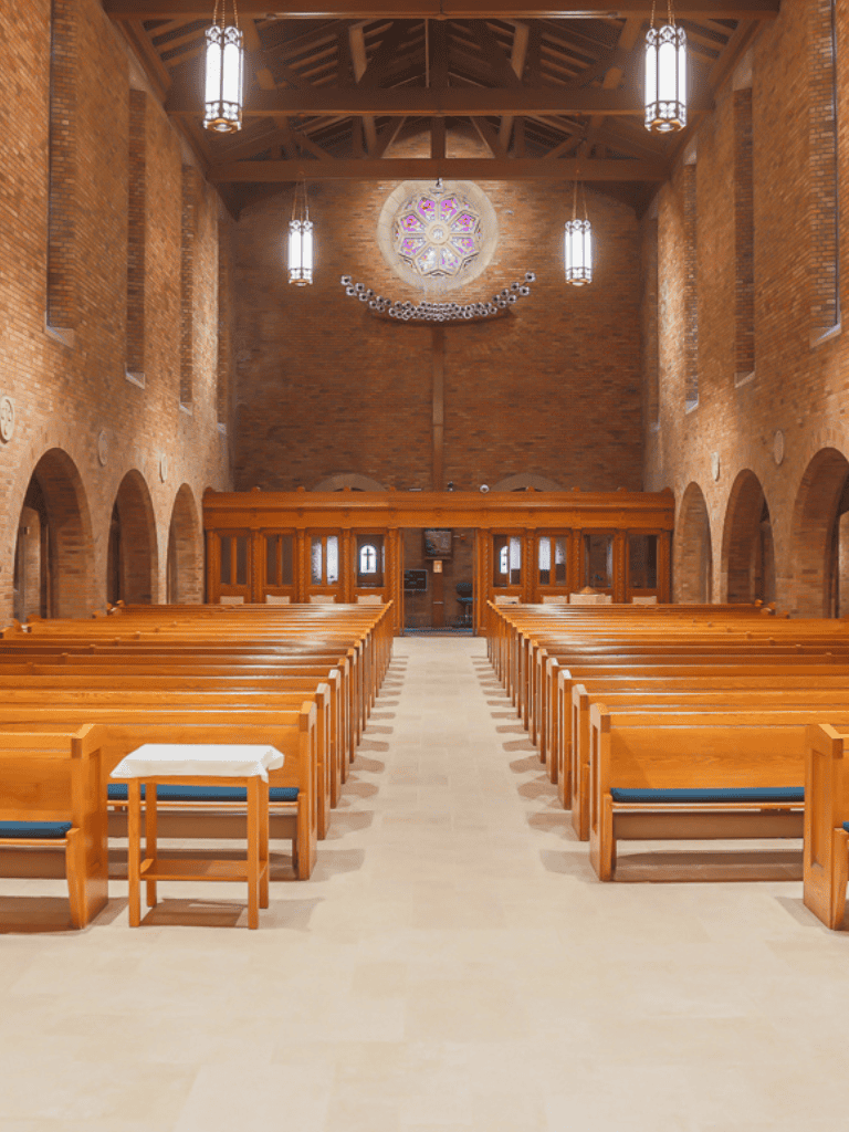 Inner view of a church with wooden pews, high brick walls, and stained glass windows, perfect for religious services and ceremonies.
