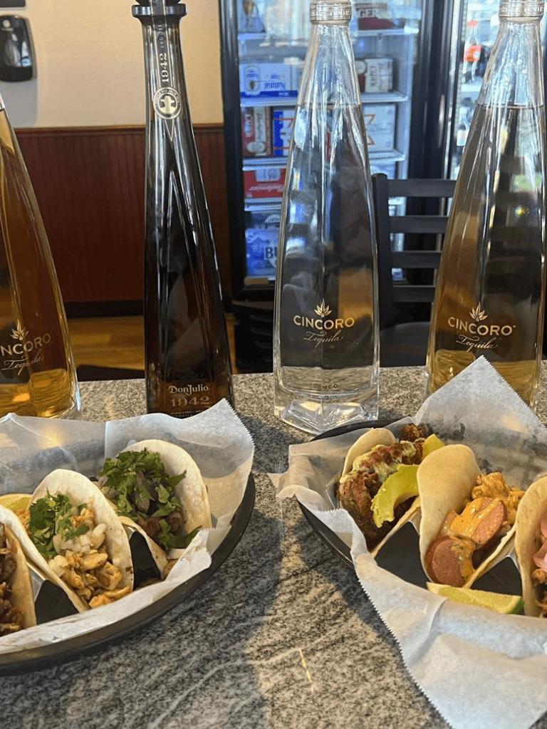 Delicious tacos with various fillings, along with bottles of Cincoro tequila on a restaurant table.