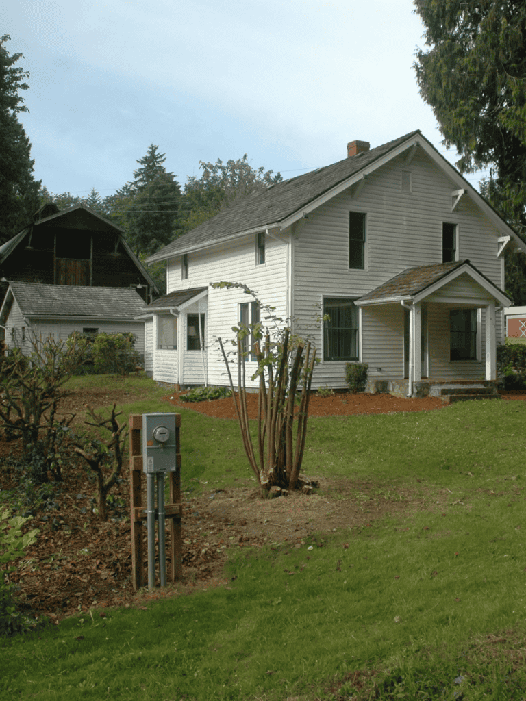 Vintage white house with landscaped yard and mature trees.