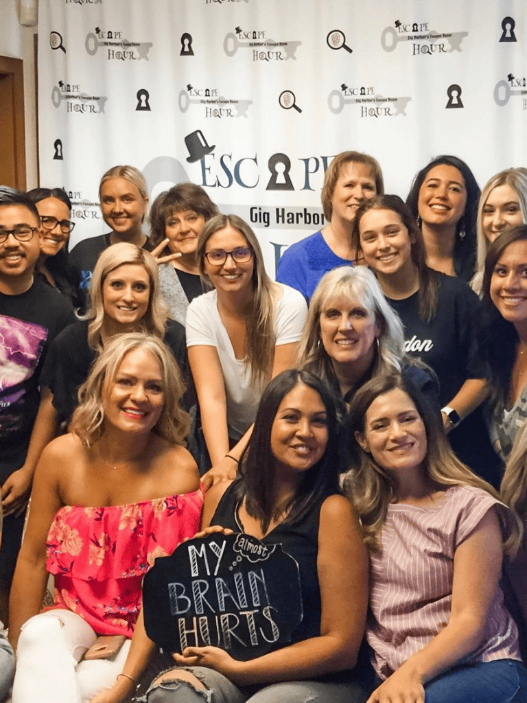 A group of diverse women and men smiling at a QuestForDirections event in front of a branded backdrop.